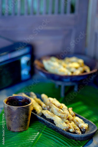 Banana fritters on a wooden plate served with a cup of water on the table with banana leaf