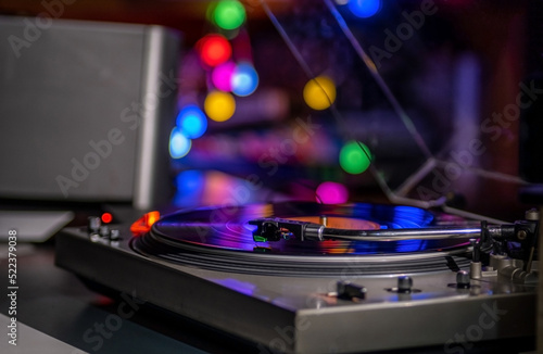 Focus on The Headshell Cartridge and Stylus of Classic Vintage Vinyl Record Player or Turntable Playing on Vinyl Record Music at night in room with colorful bokeh in background