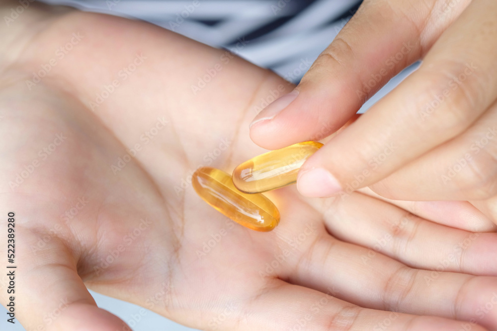 Fatty fish oil and vitamin E on the hand of a woman She will take health and wellness supplements and medical concepts.