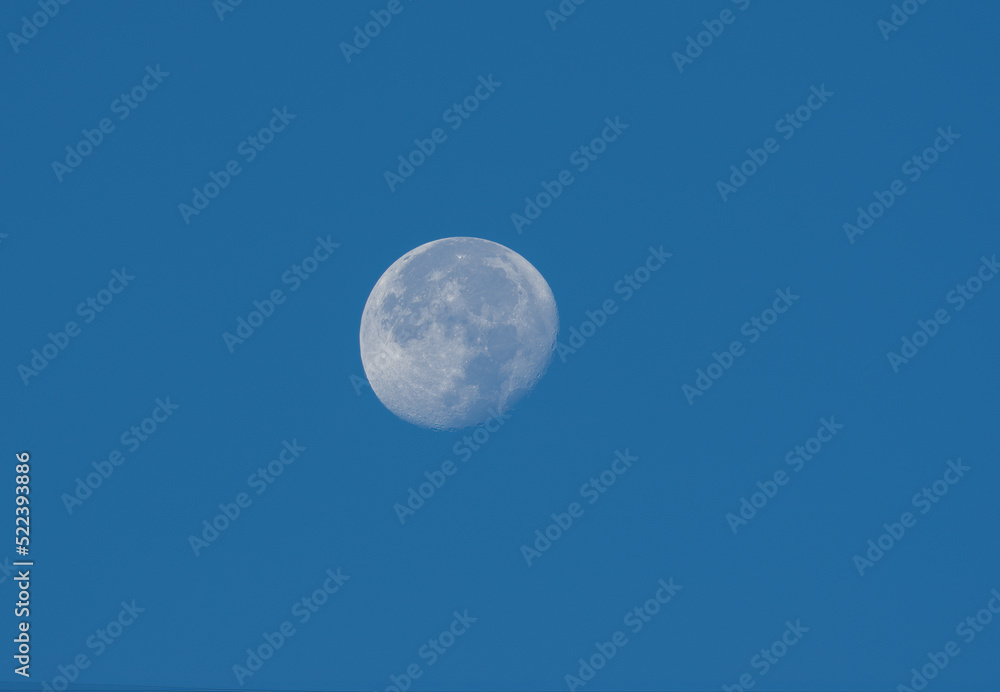 Waning gibbous moon stting against a blue morning sky.