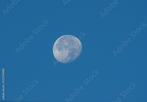 Waning gibbous moon stting against a blue morning sky.