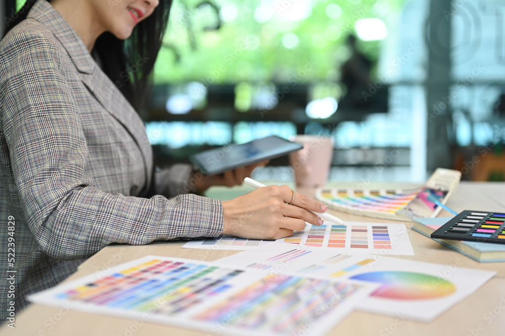 Cropped view of female interior designer using digital tablet and working with color swatches at workplace