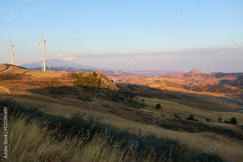 Etna smoking volcano seen from central Sicily with wind turbines in the foreground at sunset
