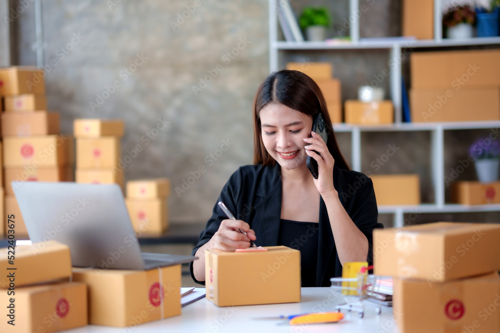 Online business owner Asian woman answering the phone talking to a customer and take note of the details of the delivery customer Negotiated address to verify correct details. Online business owner Asian woman answering the phone talking to a customer and take note of the details of the delivery customer Negotiated address to verify correct details.