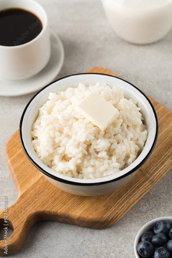 Rice porridge or pudding with a piece of butter, a mug of coffee and blueberries in a bowl. Healthy breakfast. Rice porridge or pudding with a piece of butter, a mug of coffee and blueberries in a bowl. Healthy breakfast.