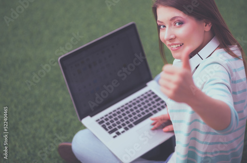 Young woman with laptop sitting on green grass