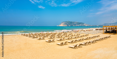Wide sandy beach with golden sand and sun loungers against a bright blue sky in Mediterranean resort of Alanya  Turkey.