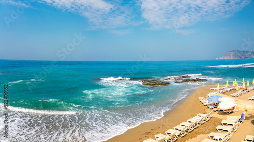 Fototapeta Naklejka Na Ścianę i Meble -  Beautiful curved line of turquoise sea surf with foam and rocks on sandy beach of a mediterranean resort.