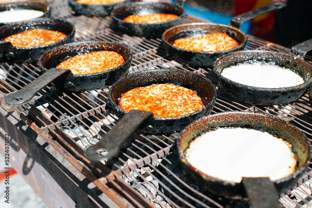 Draniki is popular dish of European cuisine. Row of cooking potato pancakes in frying pan on grill outdoors. Close-up, selective focus Draniki is popular dish of European cuisine. Row of cooking potato pancakes in frying pan on grill outdoors. Close-up, selective focus