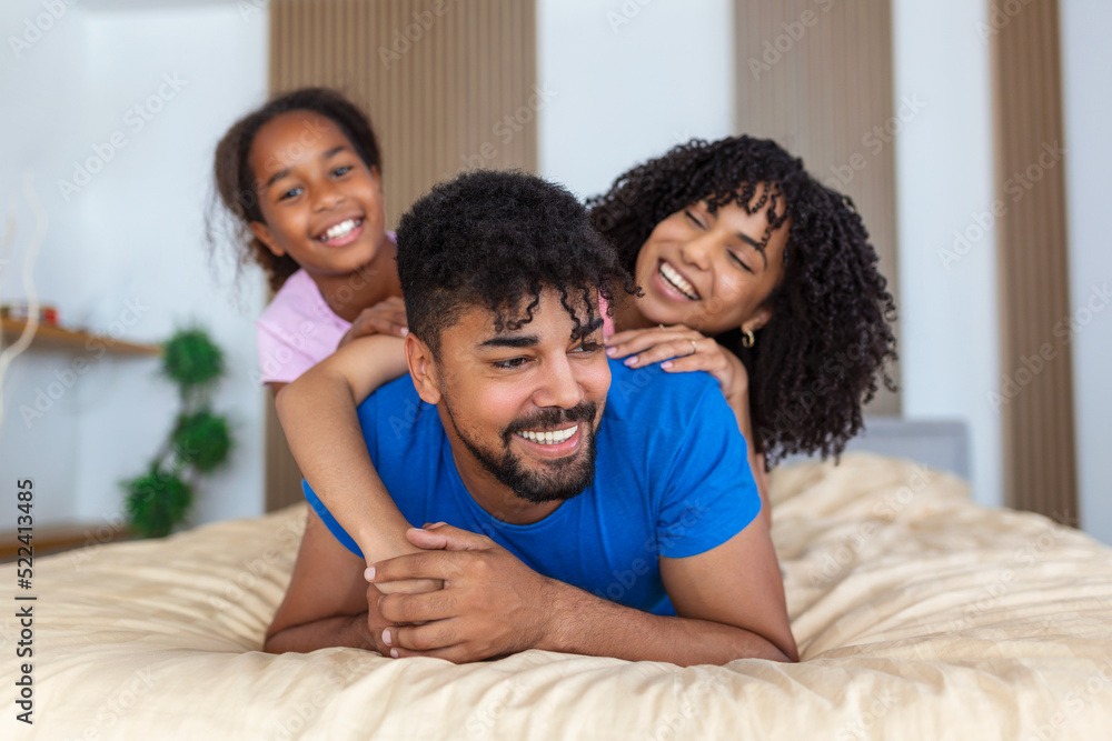 Smiling african american family of three lying on bed one on top,one in midlle and one in bottom. Smiling african american family of three lying on bed one on top,one in midlle and one in bottom.