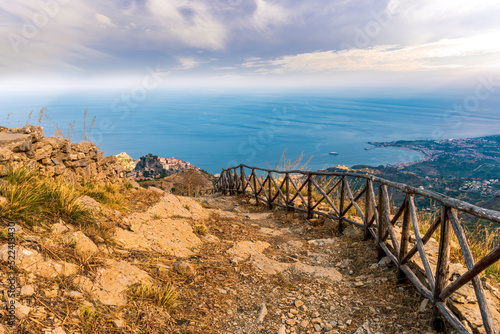 mountain landscape with a hiking trail leading to a mountain town and beautiful blue seashore far away