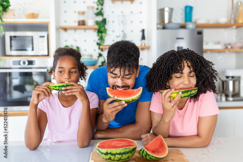 Family eats a sweet watermelon in the kitchen. A man and a woman with daughter eat a ripe watermelon in the kitchen. Happy family eating watermelon.