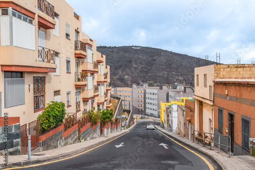 Empty street in La Laguna town with a car driving down an asphalt road, Spain. Modern buildings against the backdrop of mountains in the Canary Islands