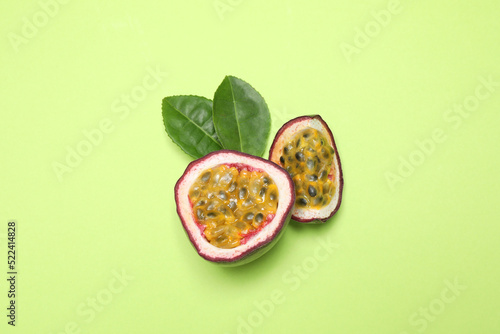 Slices of fresh ripe passion fruit (maracuya) with leaves on light green background, flat lay