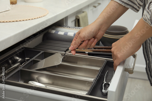 Woman taking spatula from open drawer of kitchen cabinet, closeup