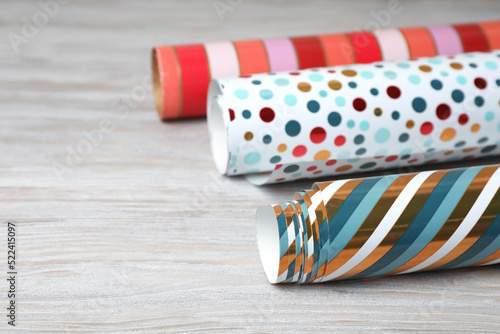 Different colorful wrapping paper rolls on white wooden table, closeup. Space for text