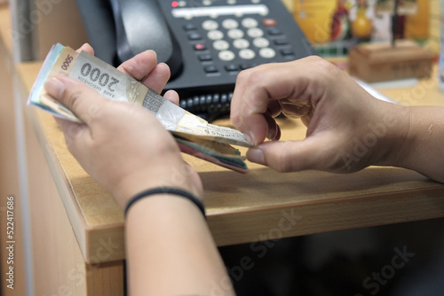 Close-up of a person's hands counting Indonesian Rupiah (IDR) banknotes on an office desk. Hands holding and counting stacks of Indonesian currency (2000 and 5000 Rupiah) in a workplace setting.
