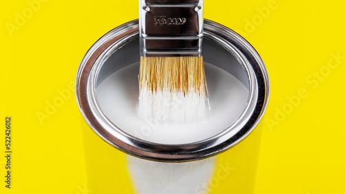 paint brush with white paint flowing into a can on yellow background close-up