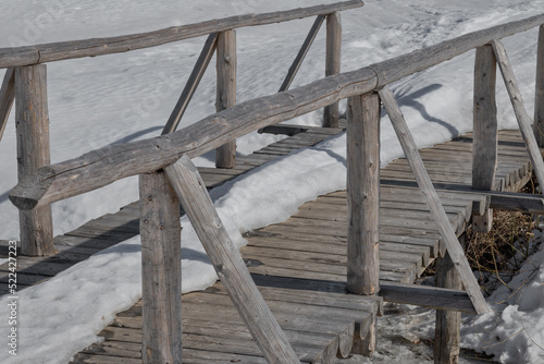 Close-up of a wooden bridge with partially melted snow in the countryside.