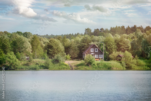 Scenic view on a recreation area with a wavy lake with reflections and a wooden house on the forest edge on the shore in the background.