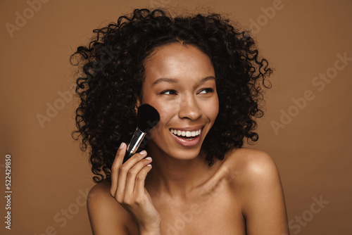 Black shirtless woman smiling and using powder brush