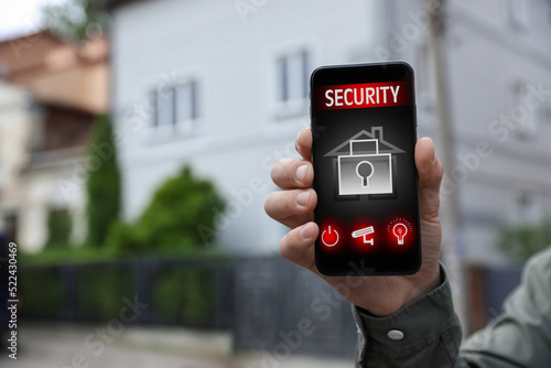 Man using home security application on smartphone in front of house outdoors, closeup