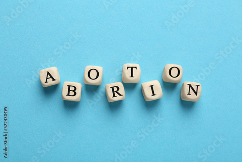 Word Abortion made of wooden cubes on light blue background  flat lay