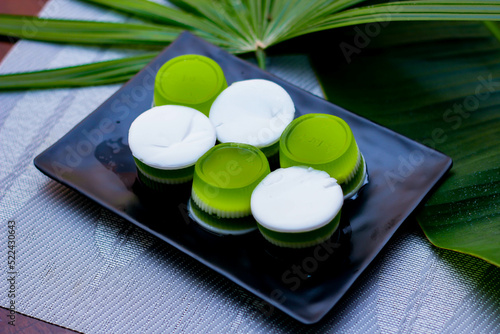 Pandan coconut milk jelly served in a black plate on a wooden table with banana leaves beside.