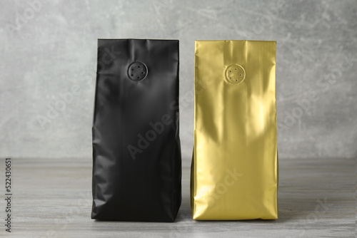 Different blank foil packages on wooden table against light grey background