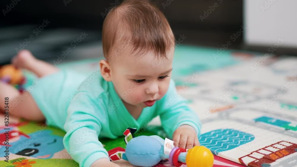 Lovely baby boy in blue romper lies on colorful mat. Cute kid playing with a toy, pulling it to his mouth and looking at it with interest. Lovely baby boy in blue romper lies on colorful mat. Cute kid playing with a toy, pulling it to his mouth and looking at it with interest.