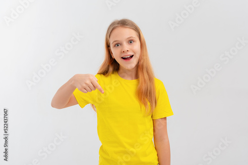 Enthusiastic teen girl smiling  pointing finger down  showing promo offer  way to store  banner or logo  standing in blank yellow tshirt over white background