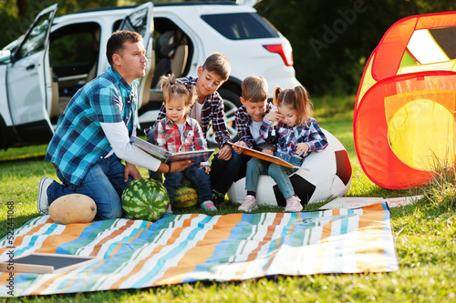 Family spending time together. Father reading book outdoor with kids against their suv car. © AS Photo Family
