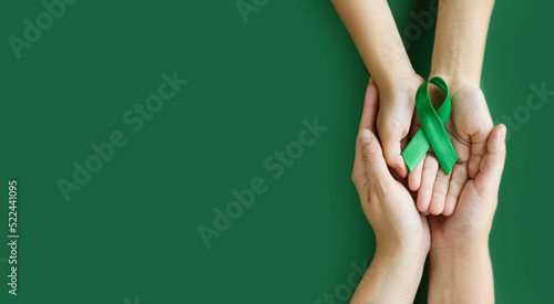 Adult and child hands holds green ribbon on green background. World lymphoma awareness day. September 15. Liver, Gallbladders bile duct, kidney Cancer and Lymphoma Awareness month.