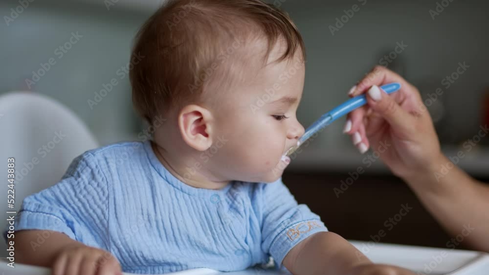 Lovely kid eating dairy sitting at the feeding table. Beautiful child nutrition from spoon. Close up.