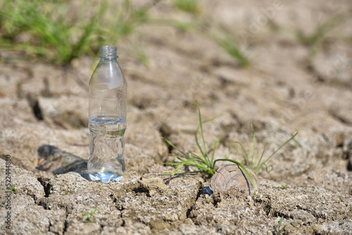 A transparent bottle of clean drinking water stands in the middle of dry, cracked desert land. Global warming concept. Drought and water crisis
