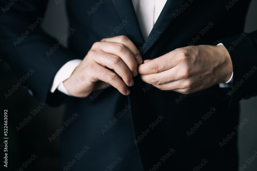 Obraz premium the groom's hands fasten his jacket in the morning before the wedding. close-up of a man in a black business suit