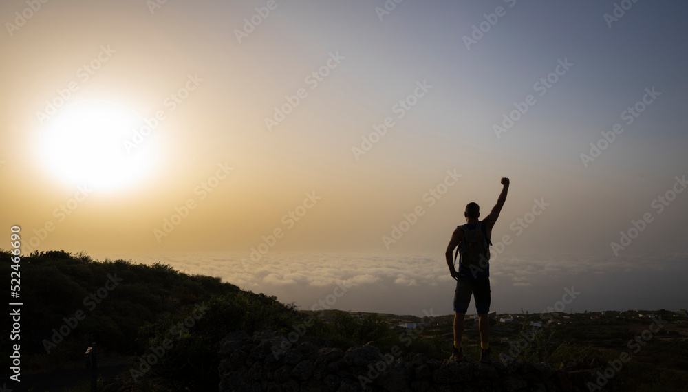 Siluette of tall male hiker on mountain above clouds in sunrise on El Hierro island in summer