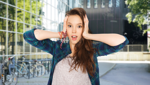emotions and education concept - stressed teenage girl holding to her head over city street or school yard background