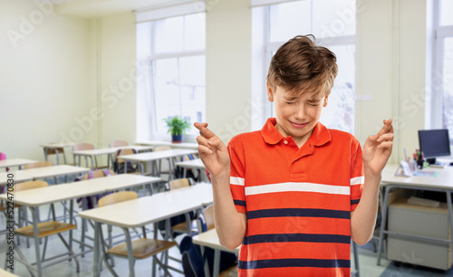 school  education and people concept - scared student boy in red polo t-shirt holding fingers crossed over empty classroom background