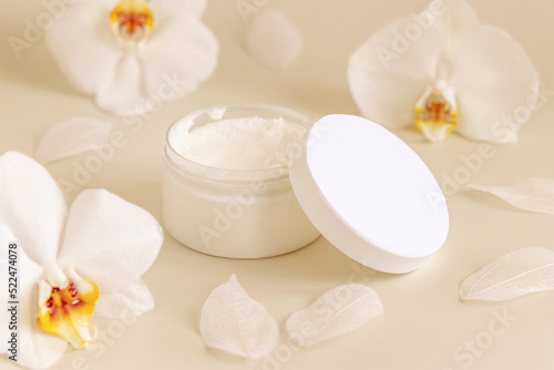 Opened Cream jar with a blank lid near orchid flowers on light yellow close up. Cosmetic Mockup