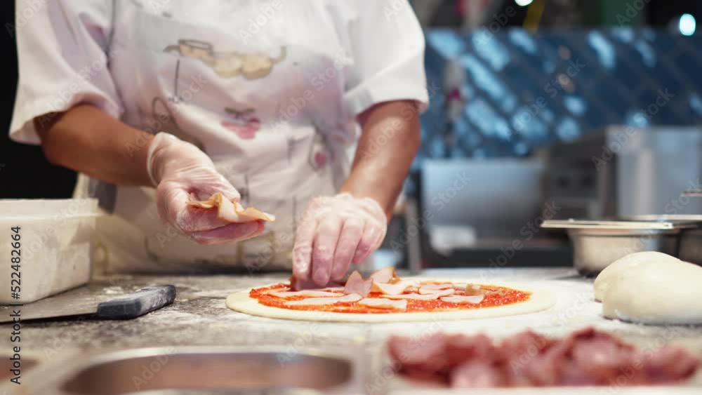 Chef prepares pizza spreads pieces of bacon on raw prepared dough, dressing preparing pizza for baking. Meat ingredients for pizza topping, Chef woman in white gloves prepares pizza
Chef prepares pizza spreads pieces of bacon on raw prepared dough, dressing preparing pizza for baking. Meat ingredients for pizza topping, Chef woman in white gloves prepares pizza