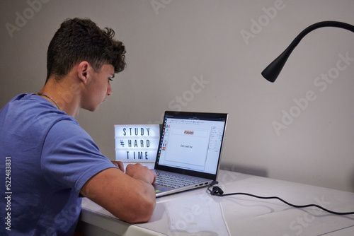 A boy working on the laptop with a lamp and a desk with text study hard time