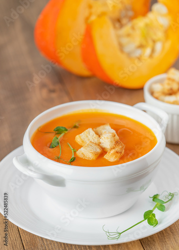 Pumpkin soup with croutons in white bowl on wooden background. Close up