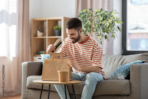 consumption, eating and people concept - smiling man unpacking takeaway food in paper bag at home