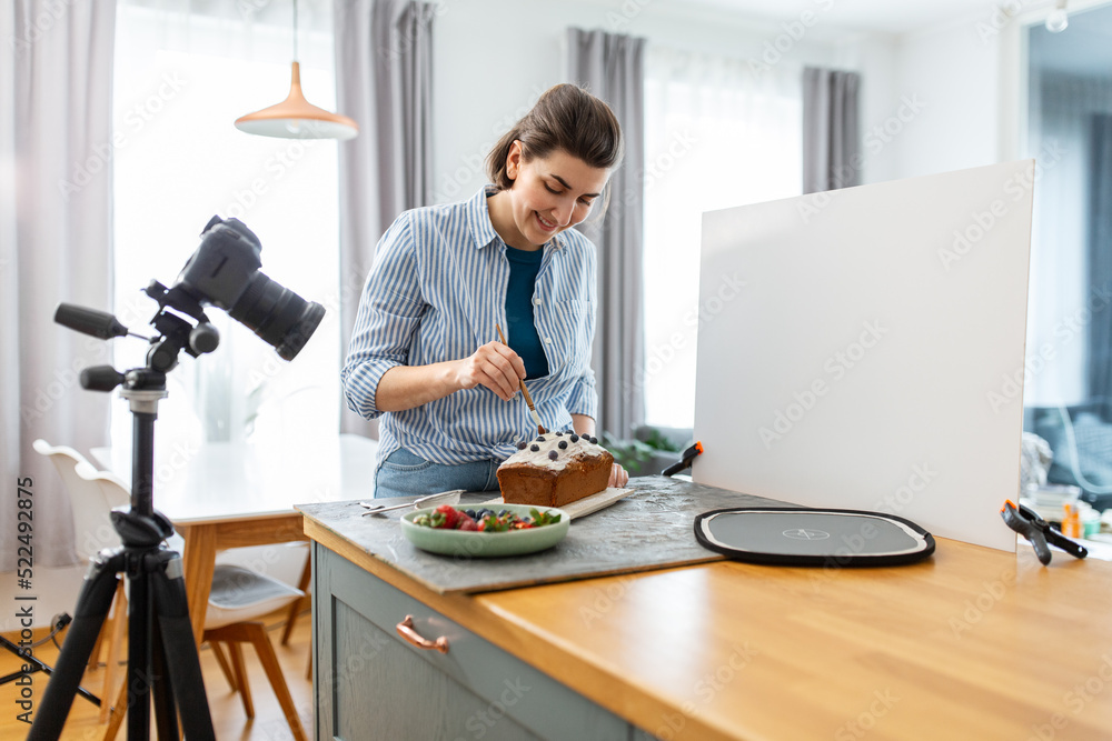 blogging, photographing and people concept - happy smiling female photographer or food blogger with camera, cake and brush working in kitchen at home blogging, photographing and people concept - happy smiling female photographer or food blogger with camera, cake and brush working in kitchen at home