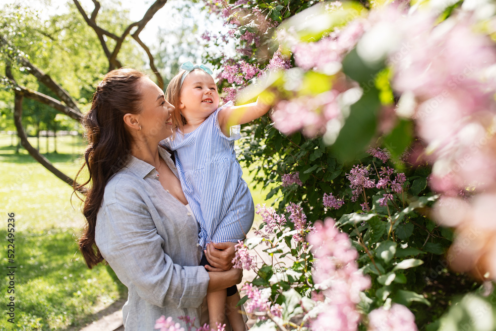 family, motherhood and people concept - happy mother with little daughter touching lilac flowers at summer park or garden family, motherhood and people concept - happy mother with little daughter touching lilac flowers at summer park or garden