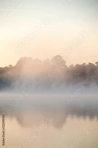 A mist drifts over the pond as the sun gradually lights the sky  the scene offering a moment of serenity and reflection.