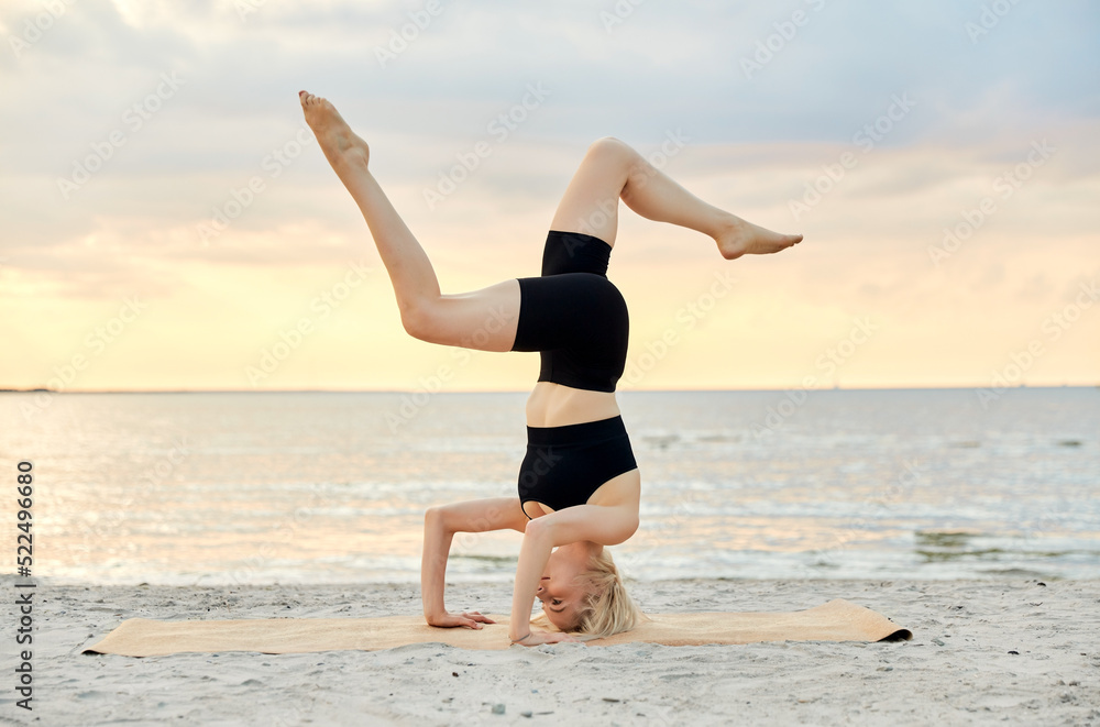 fitness, sport, and healthy lifestyle concept - woman doing yoga headstand on beach over sunset