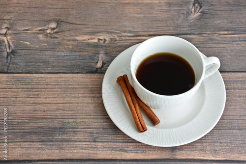 white cup of coffee with saucer and cinnamon sticks isolated on wooden background