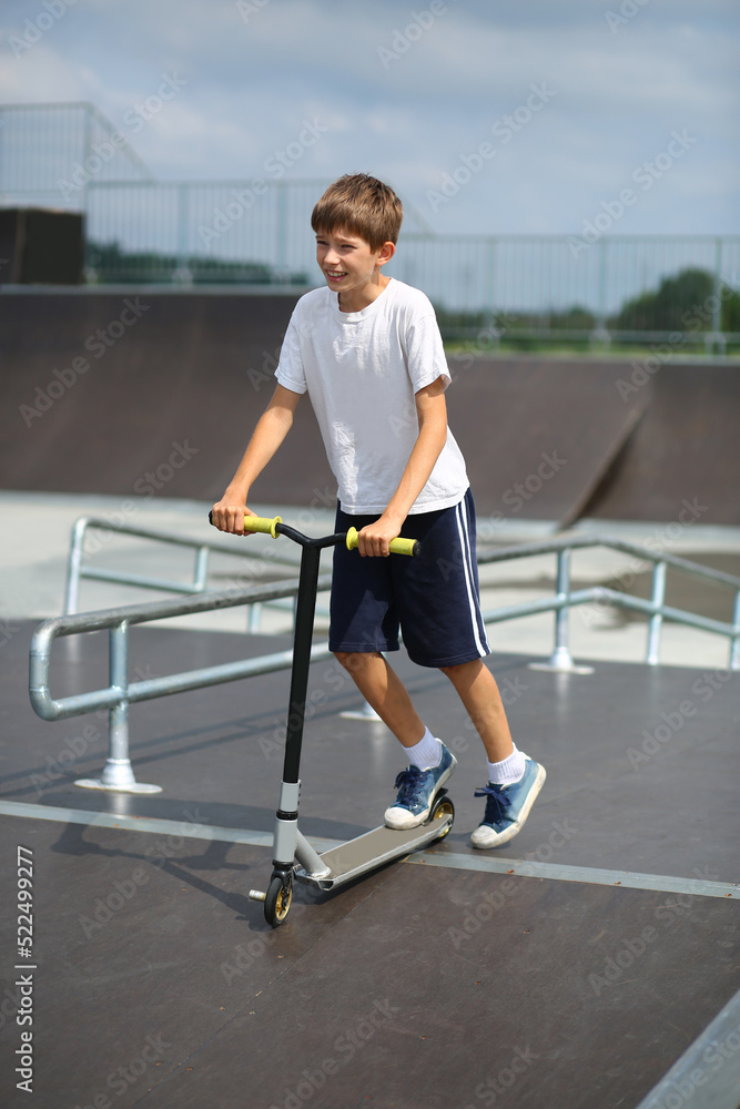 Fototapeta premium Active ten year old boy riding a scooter in the summer skate park